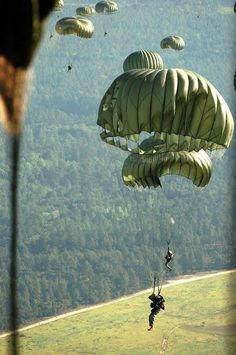 two people are parasailing in the air with parachutes above them and trees behind them