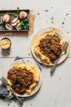 two plates with mashed potatoes topped with meat and veggies next to a pan of mushrooms