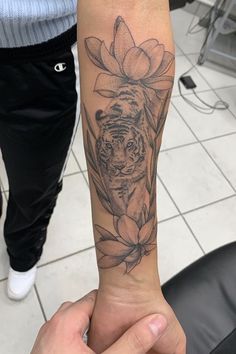 a person with a tattoo on their arm holding up a tiger and lotus flower in front of them