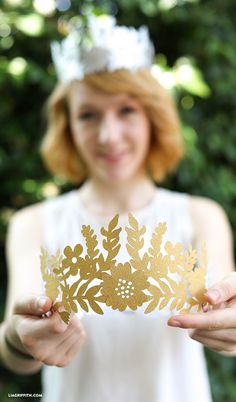 a woman wearing a tiara holding up a piece of paper with leaves on it