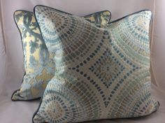 two blue and yellow pillows sitting on top of a white couch next to each other