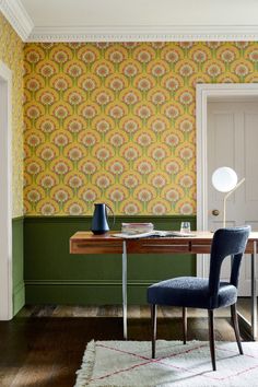 a desk with a lamp and chair in front of a wallpapered room that has green walls