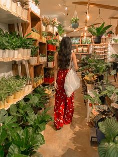 a woman in red pants walking through a store filled with plants and potted plants