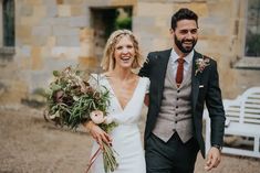 a bride and groom walking down the street holding bouquets in their hands while smiling at each other