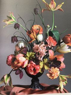 a vase filled with lots of flowers on top of a brown cloth covered tablecloth