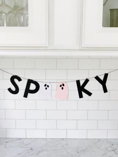 a black and pink spooky banner hanging from a kitchen counter top next to a white brick wall