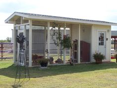 a small white shed sitting on top of a grass covered field next to a fence