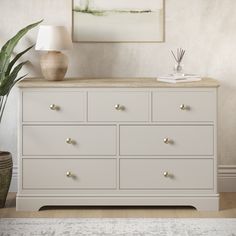 a white dresser with two lamps and a painting on the wall