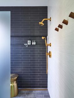 a bathroom with black tile and gold fixtures on the shower head, hand held by brass faucets