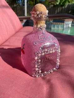 a pink bottle with pearls on it sitting on a bed next to a red pillow