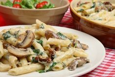 pasta with mushrooms and spinach on a white plate next to a bowl of salad