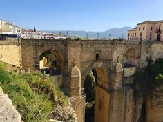 an old stone bridge spanning the width of a cliff with buildings on top and below