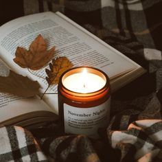 an open book sitting on top of a bed next to a lit candle and leaf