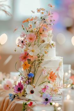 a white wedding cake with flowers on the top is surrounded by candles and confetti