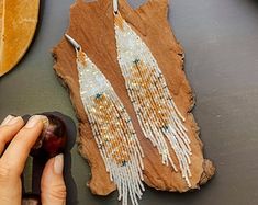 a woman is making beaded earrings on a piece of wood