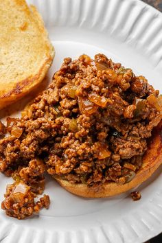 a white plate topped with a sloppy joe sandwich next to a slice of toasted bread