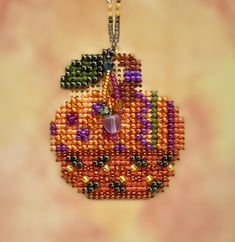 a beaded apple ornament hanging from a chain on a beige background with oranges and greens