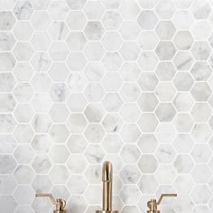 two gold faucets on a marble tiled wall in a bathroom with hexagonal tiles