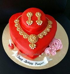 a red heart shaped cake with gold jewelry on top