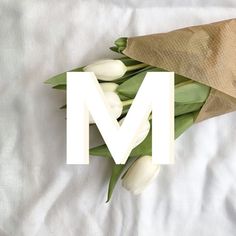 a bouquet of white tulips and the letter m on a paper bag over a bed sheet