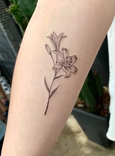 a small flower tattoo on the left arm is shown in black and grey ink,