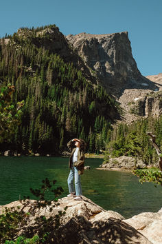 a man standing on top of a rock next to a lake