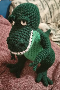 a crocheted green stuffed animal is sitting on a bed