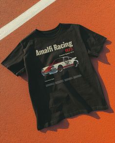 Step into the racing history of Sicily with our Amalfi Racing 1973 Tee. Inspired by the Targa Florio, this tee brings the excitement of coastal speed and vintage elegance to your wardrobe. Unisex soft cotton crew neck t-shirt featuring a Amalfi Racing Vintage Car graphic printed on the front. Fabrics: 100% cotton, 6 oz Made in: LA Casual Short Sleeve T-shirt For Motorsport Events, Racing Style T-shirt With Letter Print And Crew Neck, Casual T-shirt With Letter Print For Motorsport Events, Cotton Racing Style Top With Graphic Print, Black Graphic Print Tops For Motorsport Events, Racing Style Crew Neck T-shirt For Motorsport Events, Cotton T-shirt For Motorsport Events, Cotton Short Sleeve T-shirt For Motorsport Events, Casual Crew Neck Tops For Motorsport Events