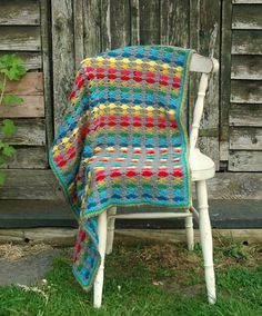 a chair with a blanket on top of it in front of a wooden wall and green grass