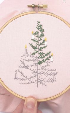 a hand embroidered christmas tree with candles on it's side, in front of a pink pillow