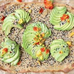 an uncooked pizza topped with avocado slices and flower petals on sesame seeds