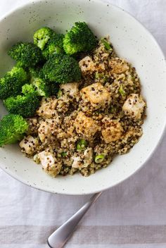 a white bowl filled with rice and broccoli on top of a table next to a spoon