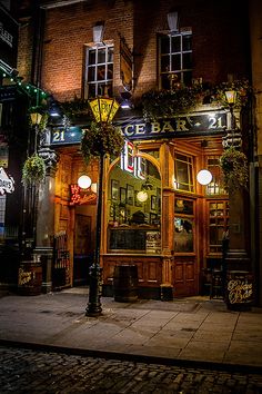 the outside of a bar lit up at night with street lights and signs on it