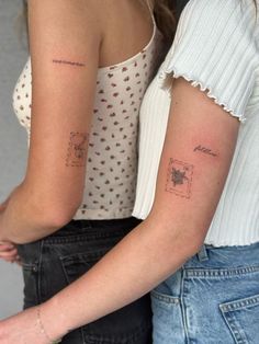 two women with matching tattoos on their arms, one is holding the other's arm