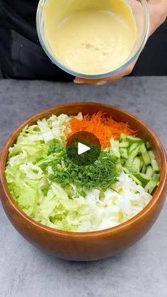 a person pouring dressing into a bowl filled with vegetables