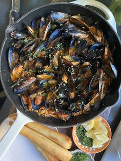 a pan filled with mussels and broccoli next to bread