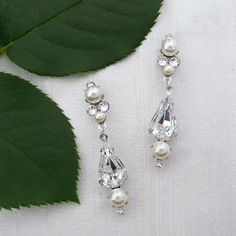 two pieces of jewelry sitting on top of a white cloth next to a green leaf