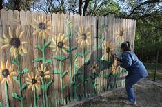 a woman painting a fence with sunflowers on it