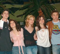 a group of young people standing next to each other in front of a palm tree