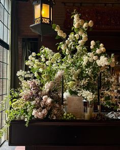 an arrangement of flowers and greenery on a table in front of a large window