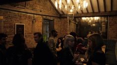 a group of people standing in a room with lights on the ceiling and brick walls