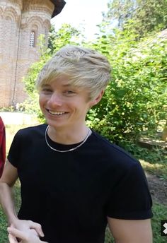 two young men standing next to each other in front of a building with trees and bushes