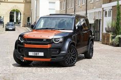 an orange and black land rover is parked in front of a brick building on a cobblestone street