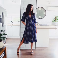 a woman standing in front of a kitchen counter with a clock on the wall behind her