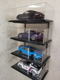 three cars in a glass case on top of black shelve shelves with white walls