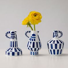 three blue and white vases with one yellow flower in it, the other two