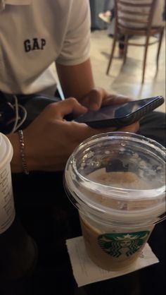 a person holding a cell phone next to a cup of coffee