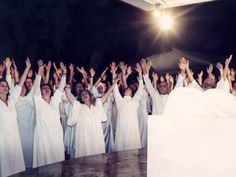 a group of people dressed in white are standing together and raising their hands to the sky