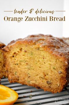 a loaf of orange zucchini bread sitting on top of a cooling rack next to an orange slice