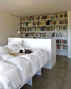 a white bed sitting in front of a book shelf filled with lots of books and cups